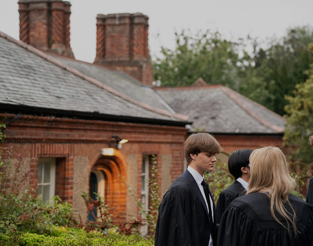 young people in academic dress stand in front of a brick building