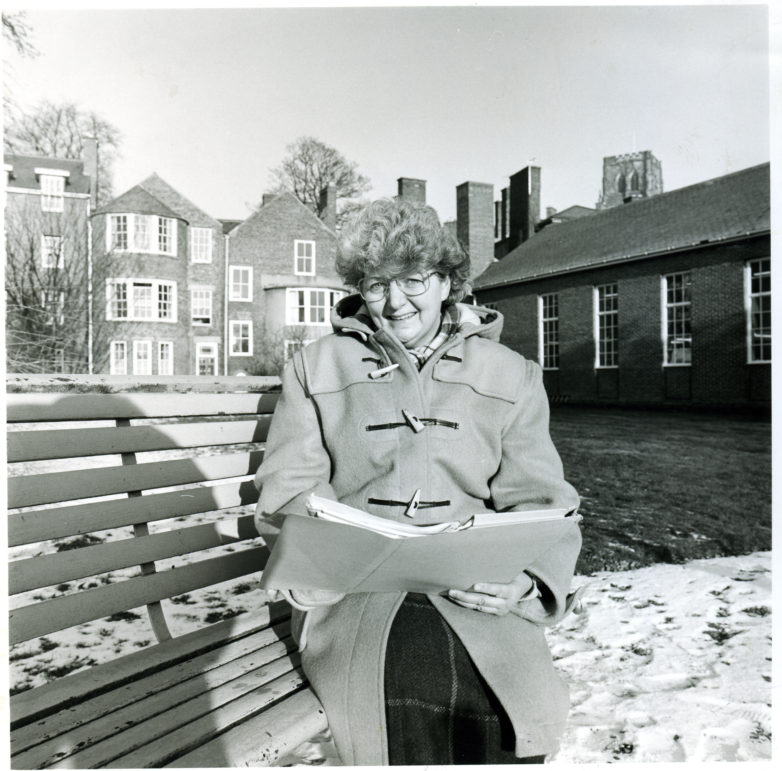 a black and white photo of a women sitting on a bench in a snowy John's garden