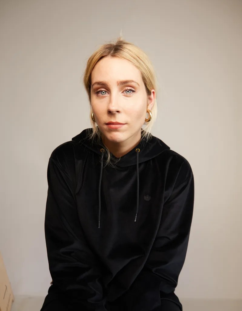A woman in black with blonde hair looks into the camera