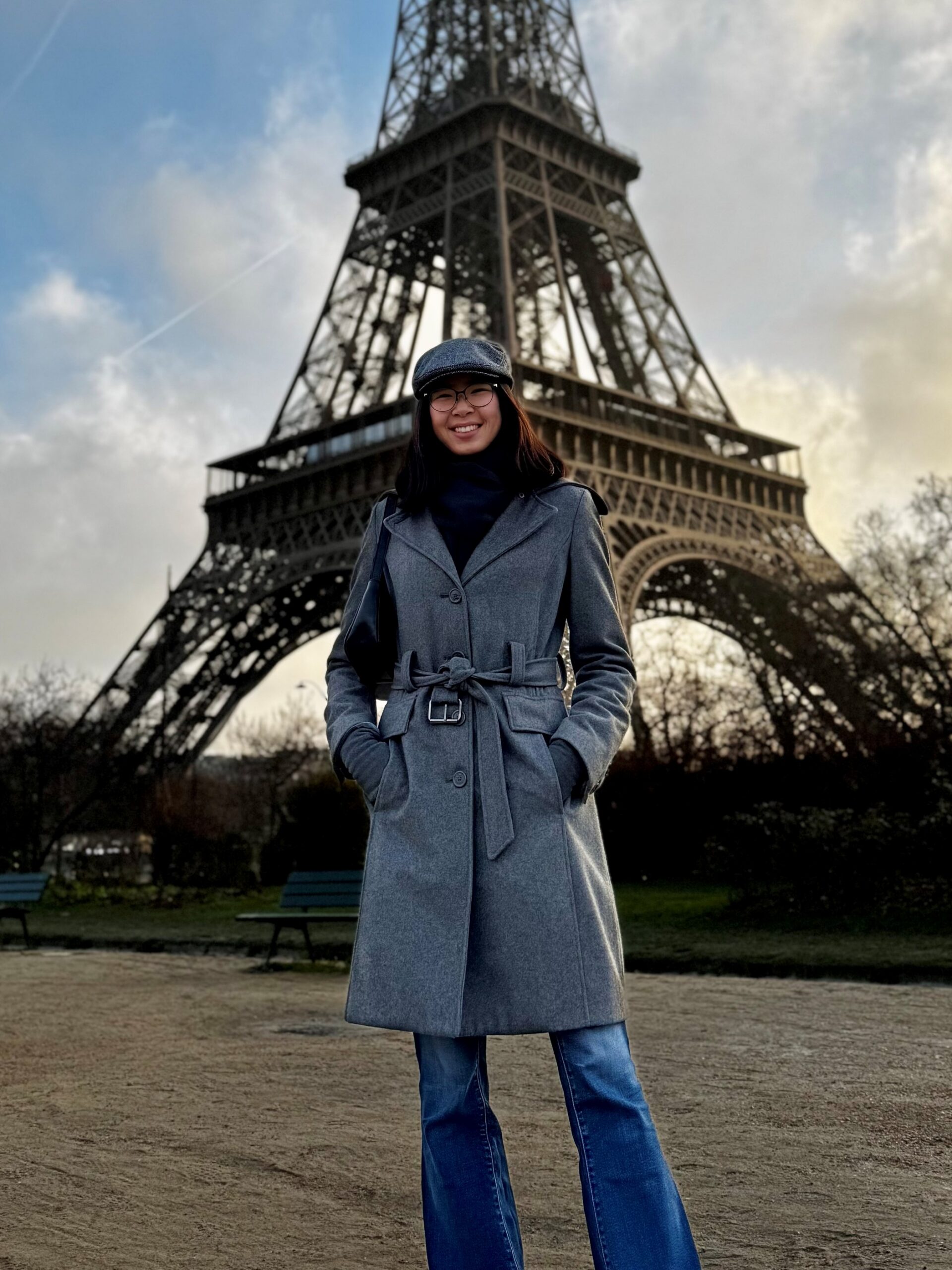 a young woman stands in front of the Eifel tower in a grey coat